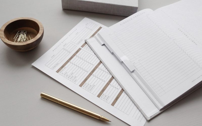 A finance tracker planner with budget sheets, a gold pen, and paper clips