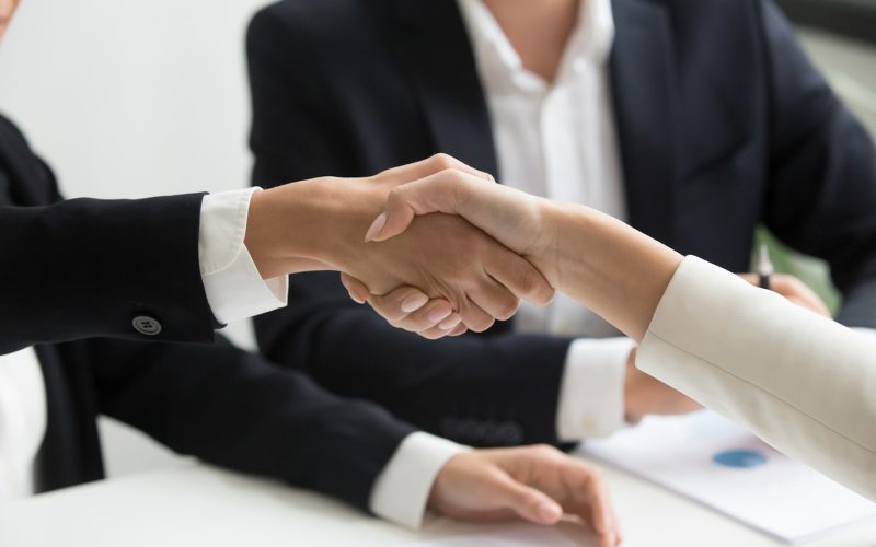 two people shaking hands in front of a laptop