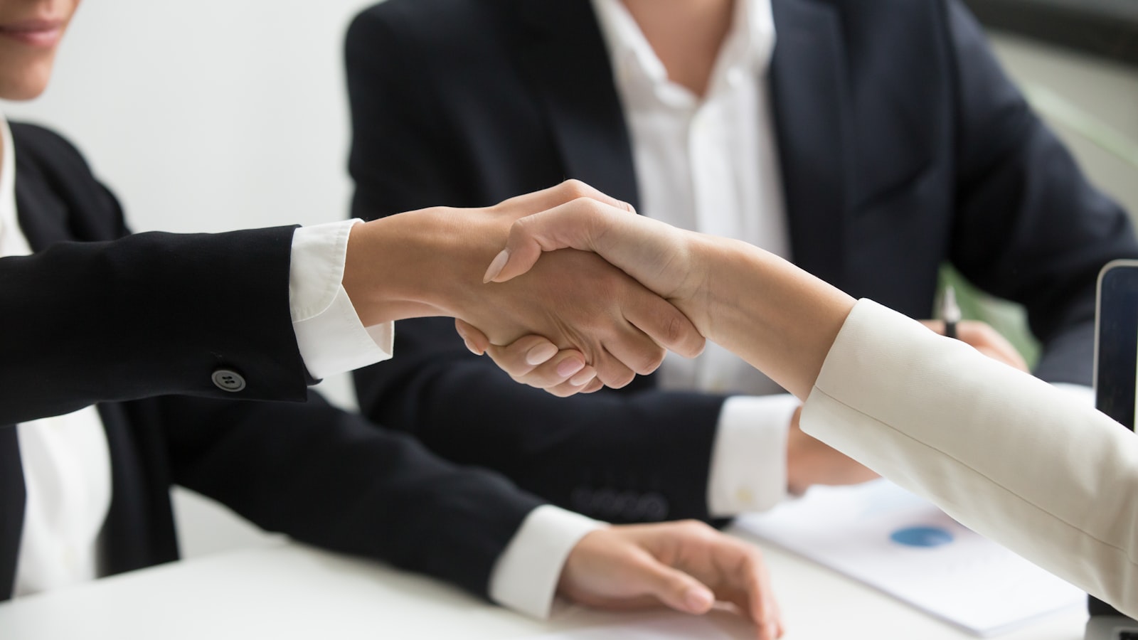 two people shaking hands in front of a laptop