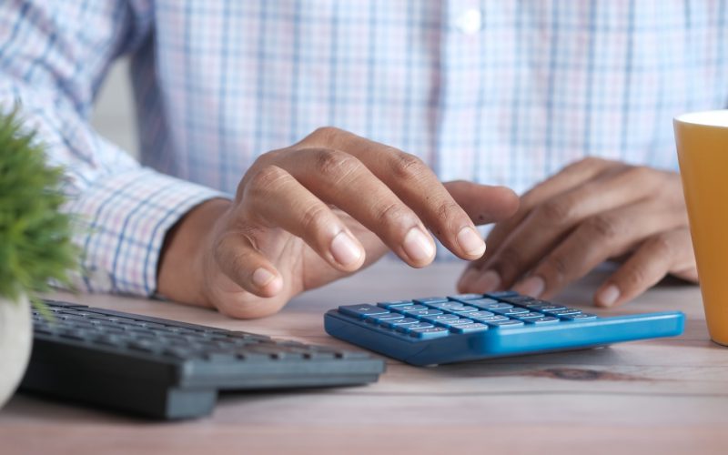 person using calculator at desk with coffee mug