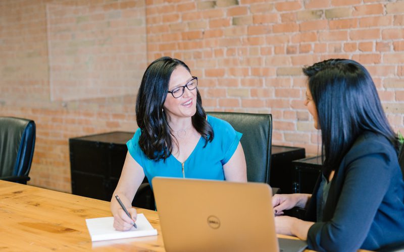 woman in teal t-shirt sitting beside woman in suit jacket