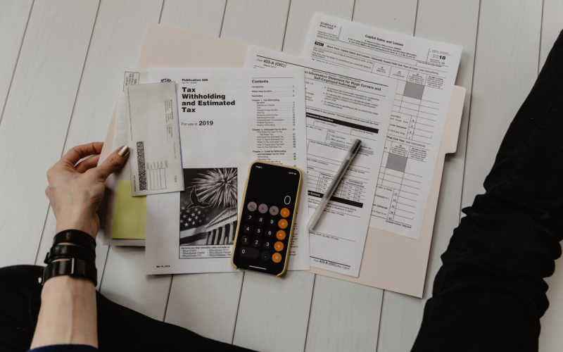 person holding paper near pen and calculator