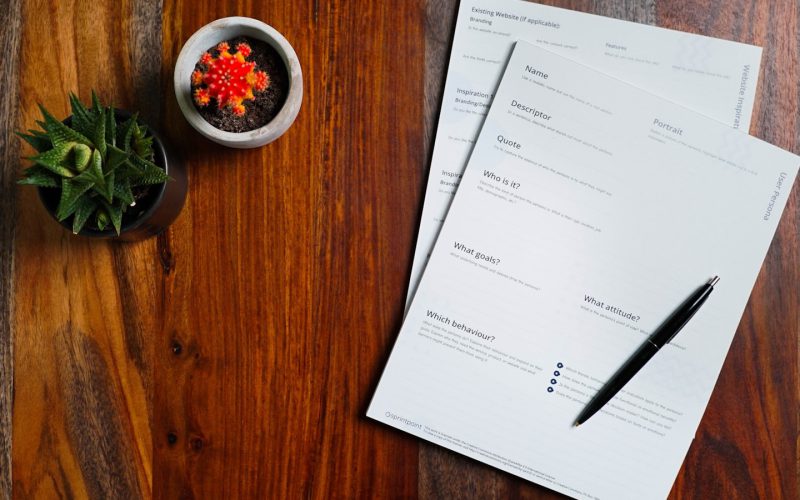 a wooden table topped with papers and a pen