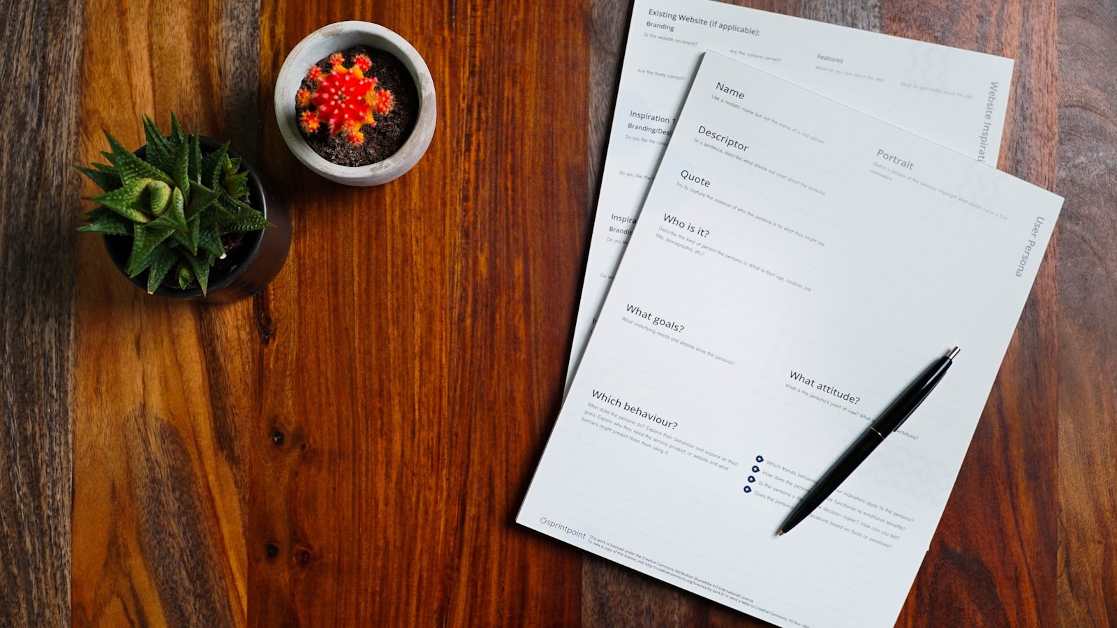 a wooden table topped with papers and a pen