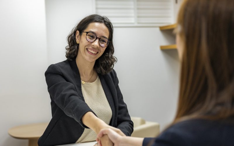a woman shaking hands with another woman sitting at a table