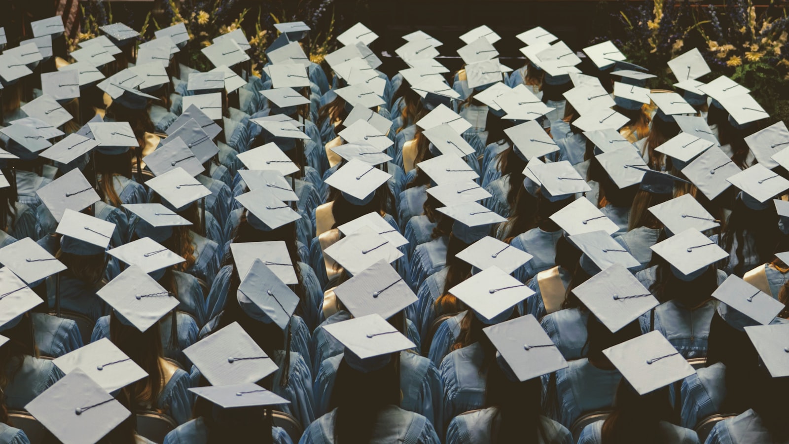 A large group of graduates in light blue gowns and caps at a ceremony