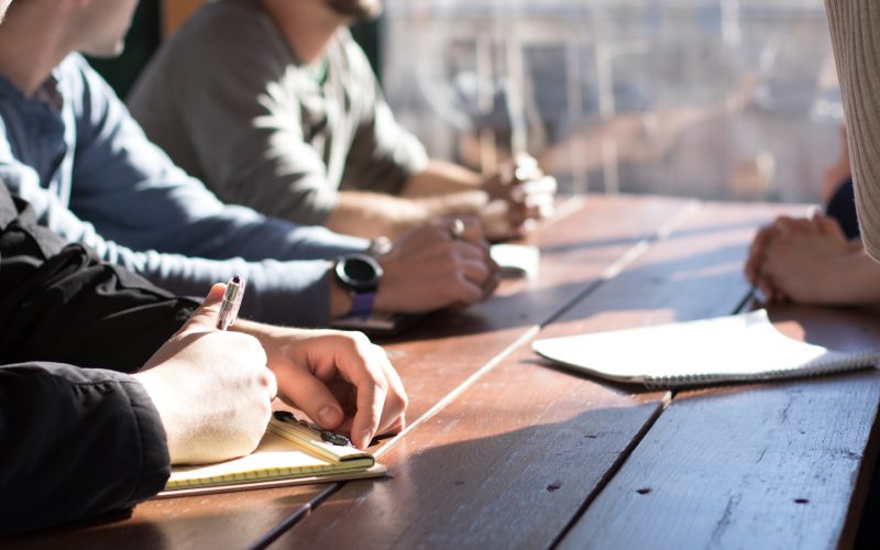 people sitting on chair in front of table while holding pens during daytime