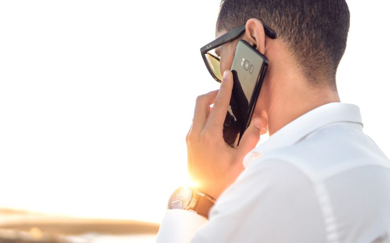 man holding smartphone standing in front of calm body of water