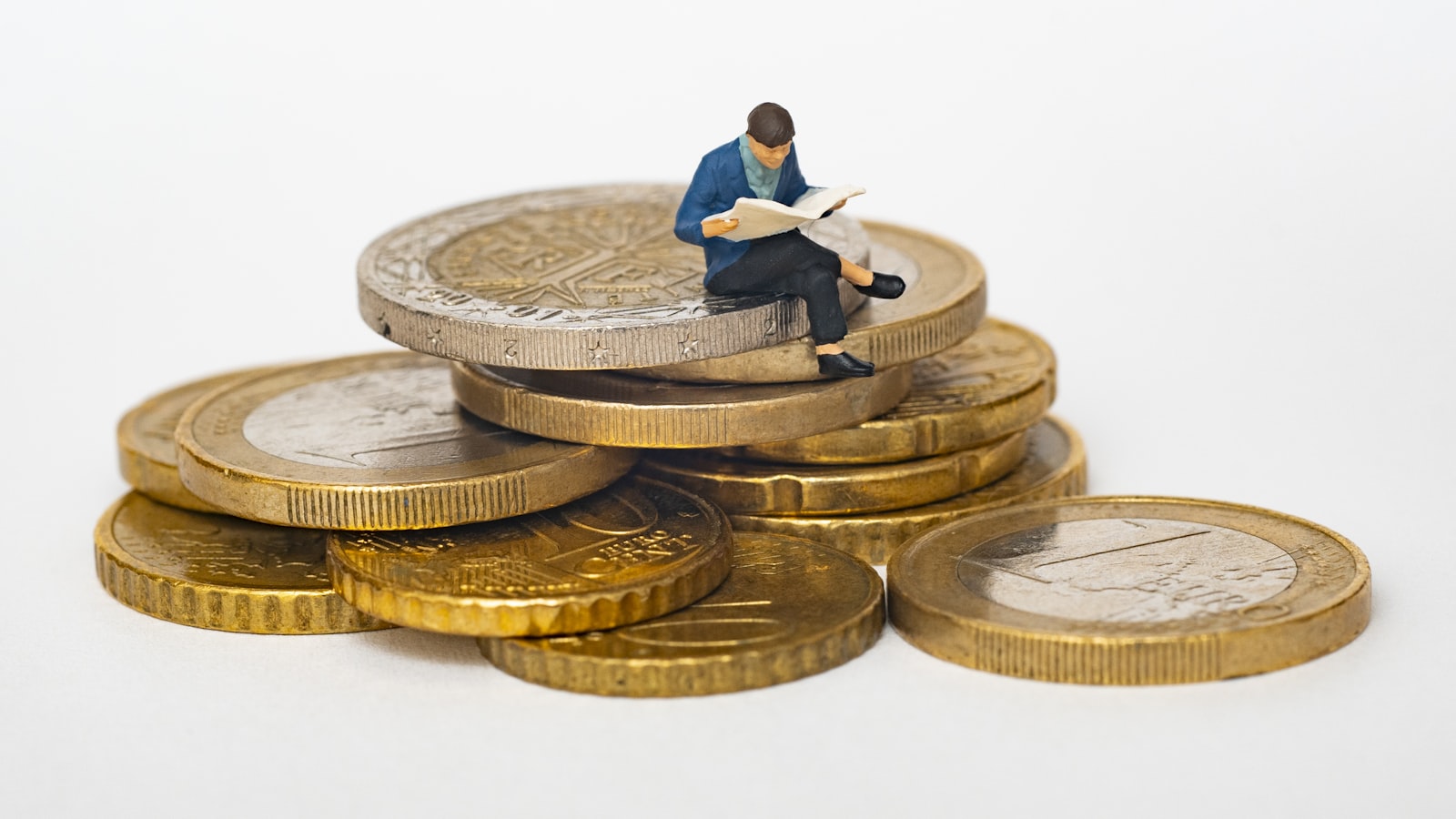 Miniature person sitting on stack of coins reading newspaper