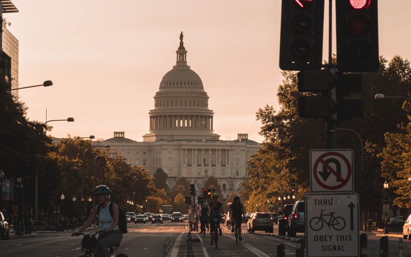 people biking on road and different vehicles viewing United States Capitol during daytime screenshot